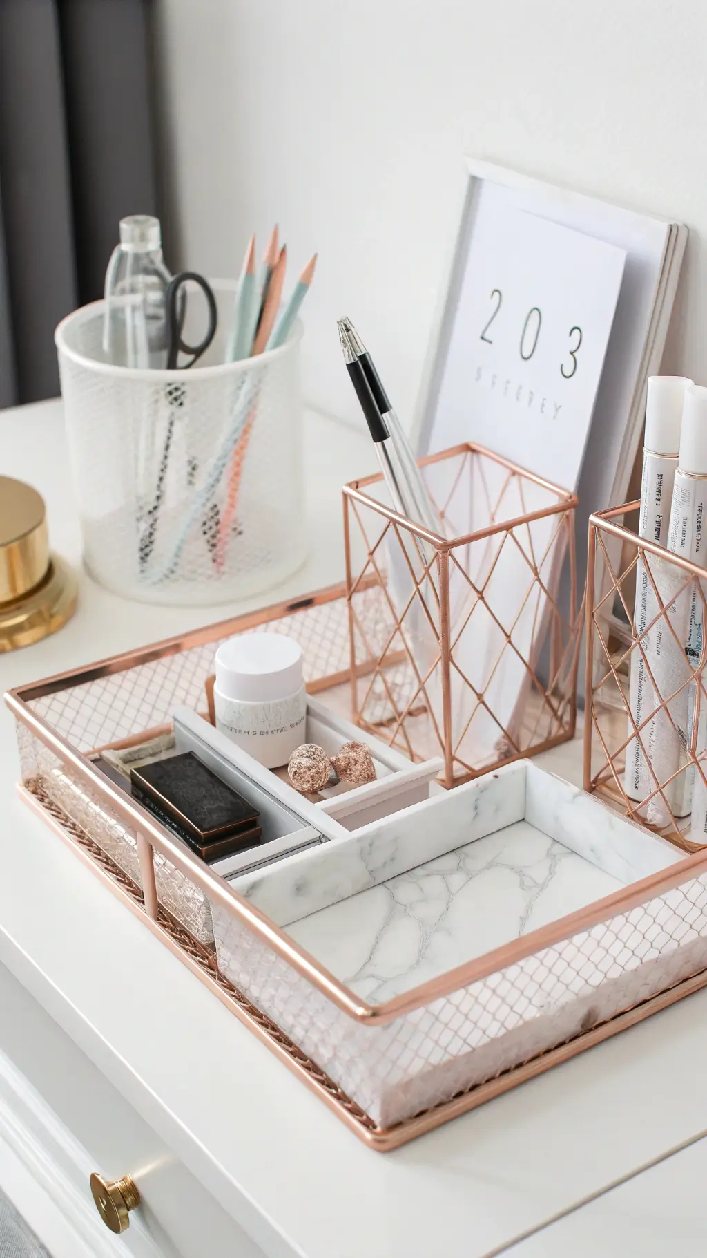 Minimalist desk with rose gold file holders, clear pen cups, white marble letter tray, and hidden storage drawers, captured with soft lighting and a gentle bokeh effect.