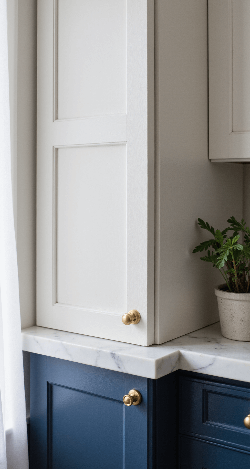 Intimate kitchen detail shot showcasing a freshly painted cabinet door with a classic white upper and deep navy lower section, featuring natural lighting, a brass pull handle, and a small potted succulent on a marble countertop, with a shallow depth of field emphasizing the paint texture.