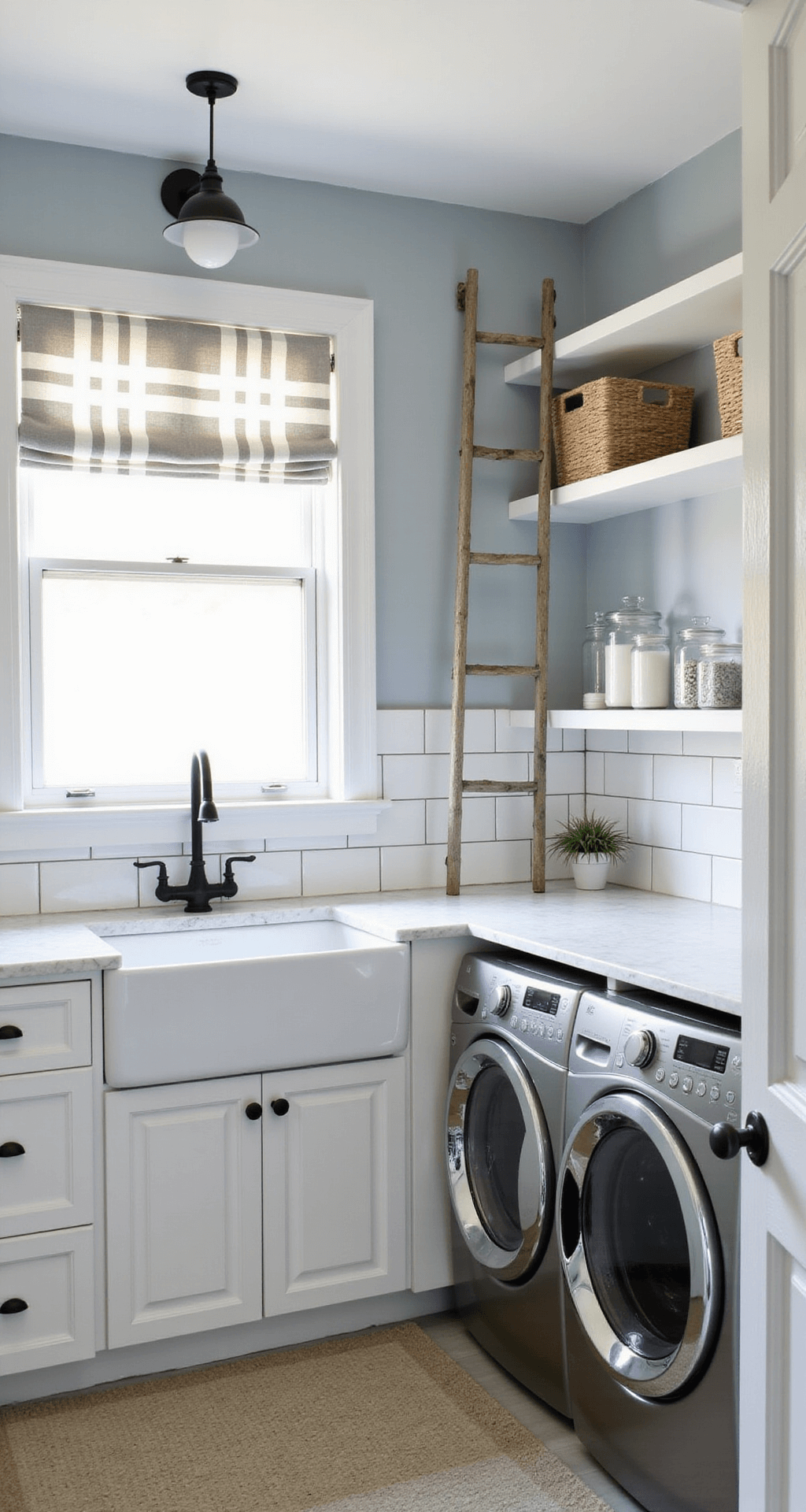 A bright modern farmhouse laundry room featuring glossy white subway tiles, pale blue-gray walls, an apron-front sink with buffalo check curtains, shaker cabinets, stainless steel washer and dryer, a marble-look countertop, open shelving with baskets and canisters, and a rustic ladder for drying clothes.