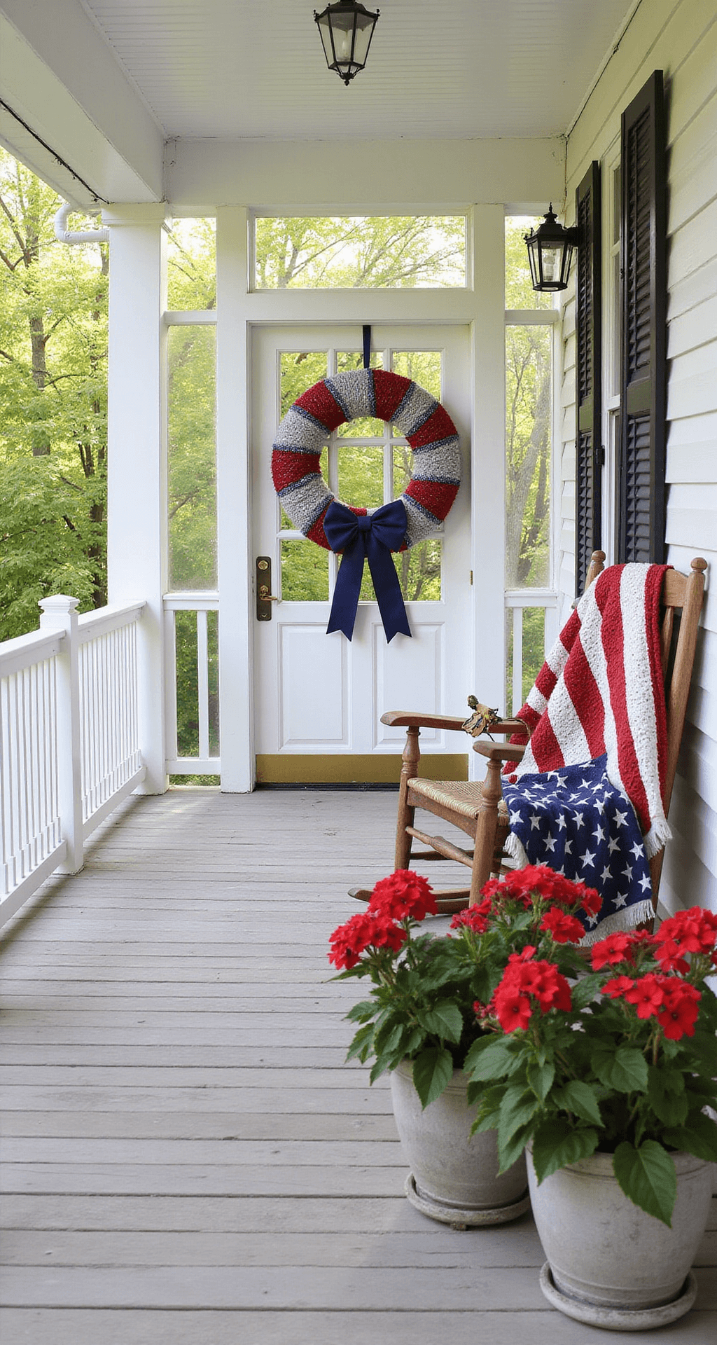 A sun-drenched front porch featuring rustic wooden floorboards, a white railing with a handmade red, white, and blue wreath adorned with glitter stars and a navy bow, a weathered rocking chair draped with an American flag quilt, and potted red geraniums by the door, creating a warm, inviting patriotic atmosphere.