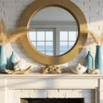An elegant coastal living room at golden hour, featuring a white limestone fireplace mantle adorned with coral and blue glass vessels, a large brass mirror, and textured decor, captured in soft natural light.