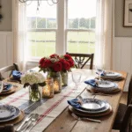A rustic farmhouse dining room set for a patriotic gathering, featuring a wooden table with a white linen tablecloth, red and navy striped runner, floral arrangements in Mason jars, vintage lanterns, elegant place settings with American flag accents, and a handcrafted star garland, all illuminated by warm golden hour light.