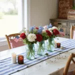Cinematic wide shot of a sunlit farmhouse dining table with a patriotic centerpiece of antique mason jars filled with red roses, white daisies, and blue hydrangeas, accented by American flags and mercury glass votives, surrounded by rustic chairs and vintage Coca-Cola crates, all set against shiplap walls and an antiqued American flag.