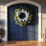 A photorealistic entryway featuring a navy blue arched door adorned with a large hydrangea wreath, complemented by a weathered oak console table with a white vase of lavender, all bathed in golden sunlight.