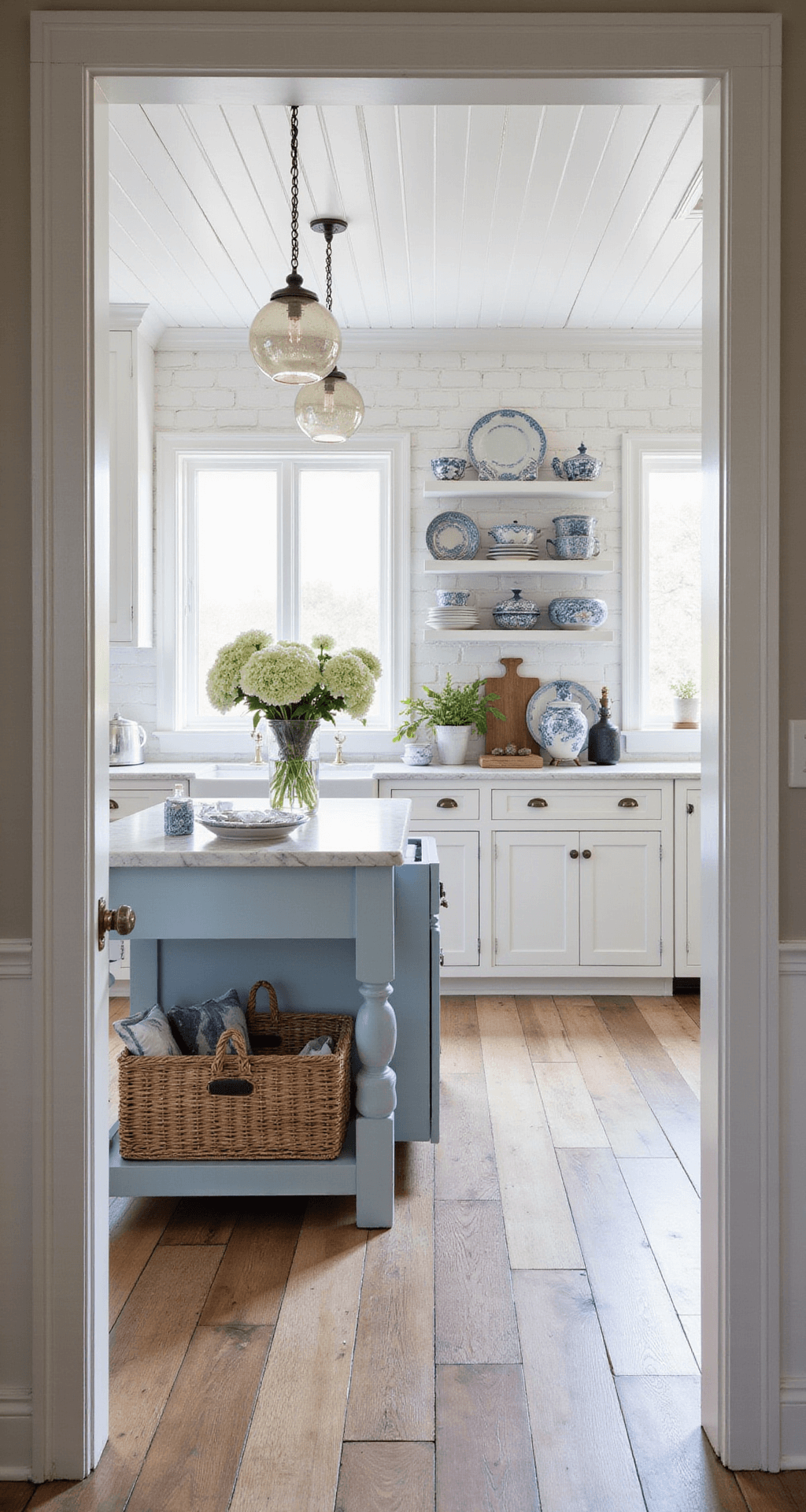 A coastal farmhouse kitchen with shiplap ceiling and white brick walls, featuring a pale blue island, vintage glass pendants, open shelving with blue-and-white ceramics, and wide-plank white oak flooring, shot in morning light from the doorway.