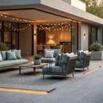 Photorealistic image of a modern patio during golden hour, featuring a premium aluminum conversation set with graphite-finished sofas and sage green cushions, illuminated by integrated LED lights and string lights, with a geometric outdoor rug and minimalist planters in the background.