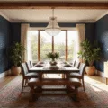 Cinematic wide-angle shot of a beautifully transformed dining room featuring a raw-edge walnut table, mixed seating, vintage Persian rug, and a crystal chandelier, all illuminated by golden hour light through large windows.
