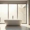 A serene minimalist bathroom featuring a freestanding white porcelain tub, light grey porcelain tiles, and a floating white oak vanity, all illuminated by soft morning sunlight through a frosted window.