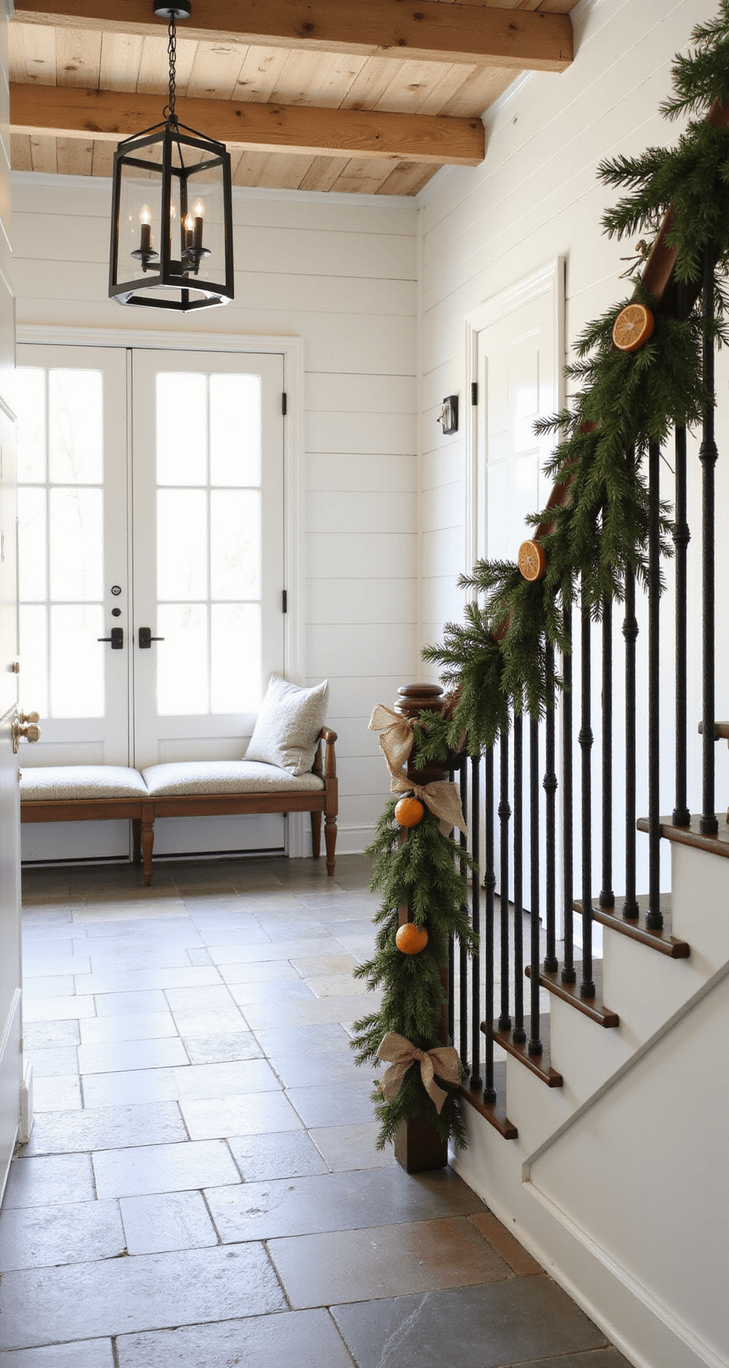 Mastering Christmas Garland Decor: Your Ultimate Styling Guide A bright modern farmhouse entryway with 12-foot ceilings and exposed wooden beams, featuring a Dutch door that lets in natural light. A rustic garland made of pine branches, dried orange slices, cinnamon sticks, and burlap bows drapes along a raw iron stair railing. The space has whitewashed shiplap walls, slate floor tiles, and a vintage bench adorned with wool throws, captured from above the stairs to highlight the garland's sweeping curve, exuding warm and inviting country charm.