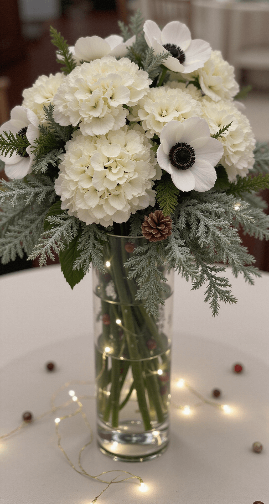 Christmas Wedding Centerpieces That'll Make Your Guests Stop Mid-Bite A winter wedding centerpiece featuring lush white hydrangeas, black-centered white anemones, silver dollar eucalyptus, frosted ferns, scattered pinecones, and fresh cranberries, illuminated by delicate LED fairy lights in a crystal-clear vase, captured from a low angle to highlight the intricate layers and soft ambient lighting.