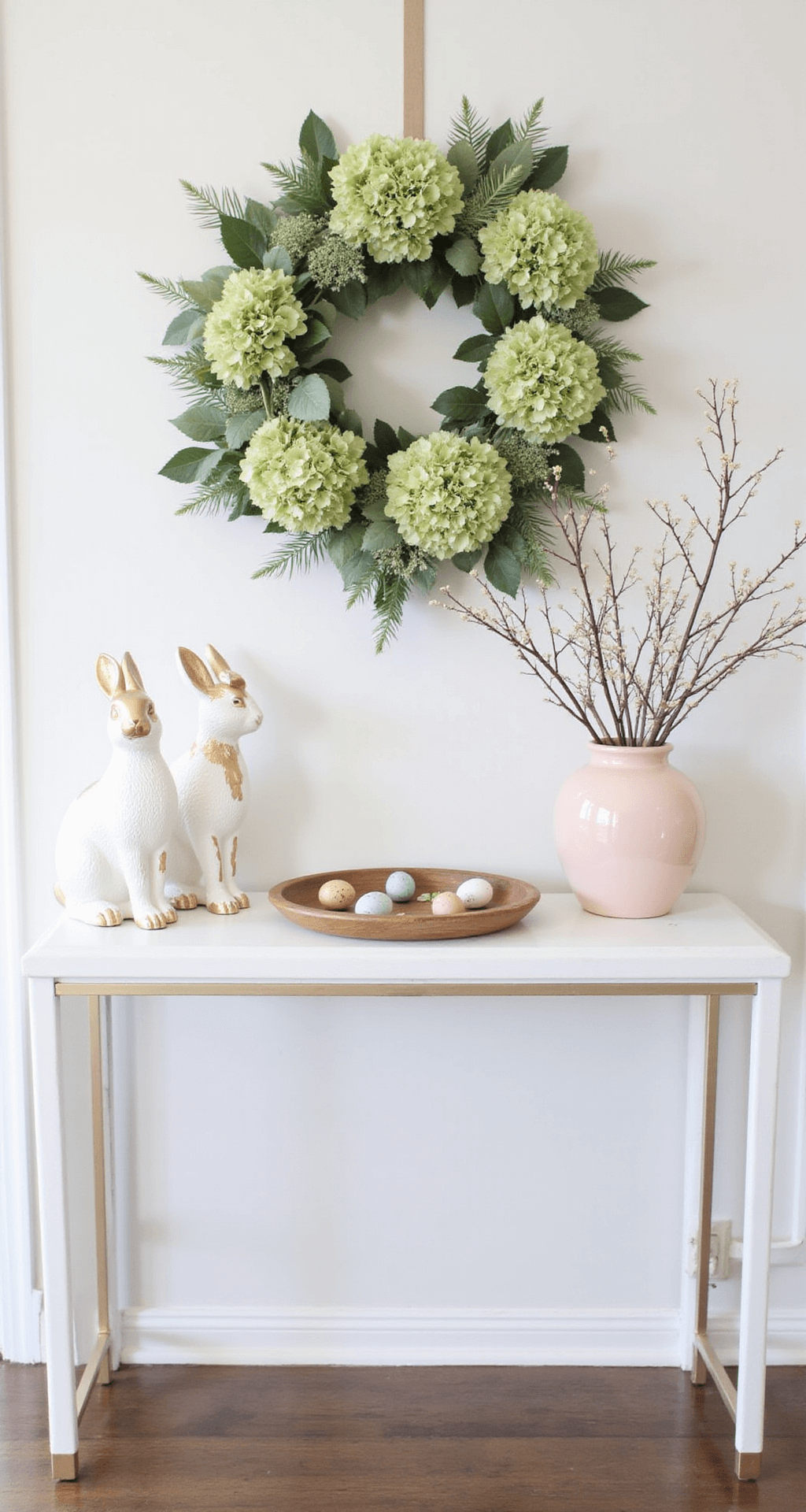 Easter Home Décor That'll Make Your Neighbors Jealous (Without Breaking the Bank) A modern entryway featuring a spring floral wreath of hydrangeas and greenery above a white console table, adorned with two asymmetrically placed white and gold bunny statues, a tray of painted eggs, and a blush pink vase with spring branches, all bathed in natural light.