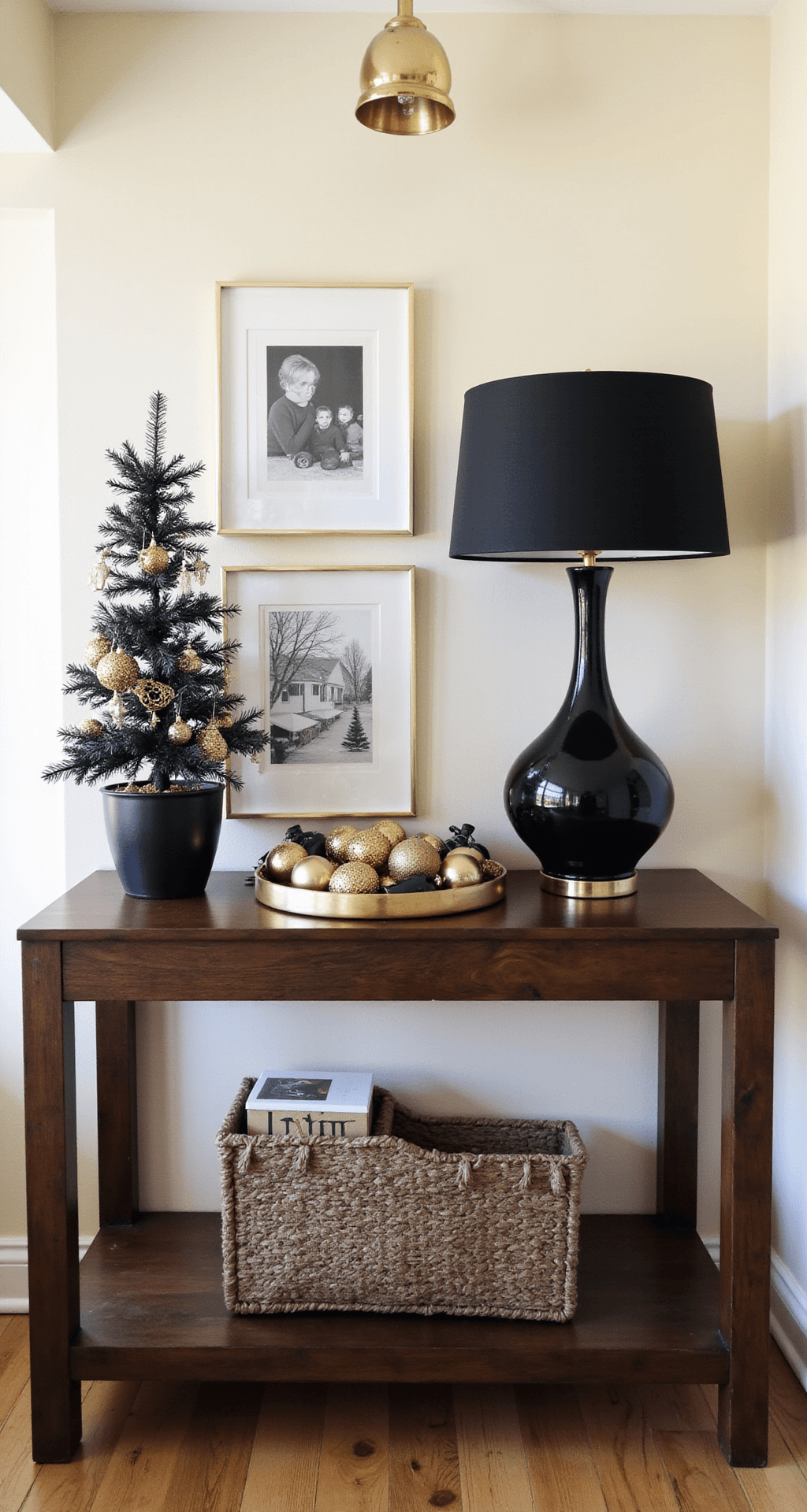 Black and Gold Christmas Decor: Your Guide to Creating a Show-Stopping Holiday Look Stylish Christmas vignette in a grand entryway featuring a 6-foot dark walnut console table against a cream wall. The scene includes a statement black ceramic lamp with a gold interior, a circular gold tray with diverse textured ornaments, a small flocked tree in a black vase with gold accents, and asymmetrically arranged black-and-white holiday photography in gold frames, all illuminated by natural afternoon light.