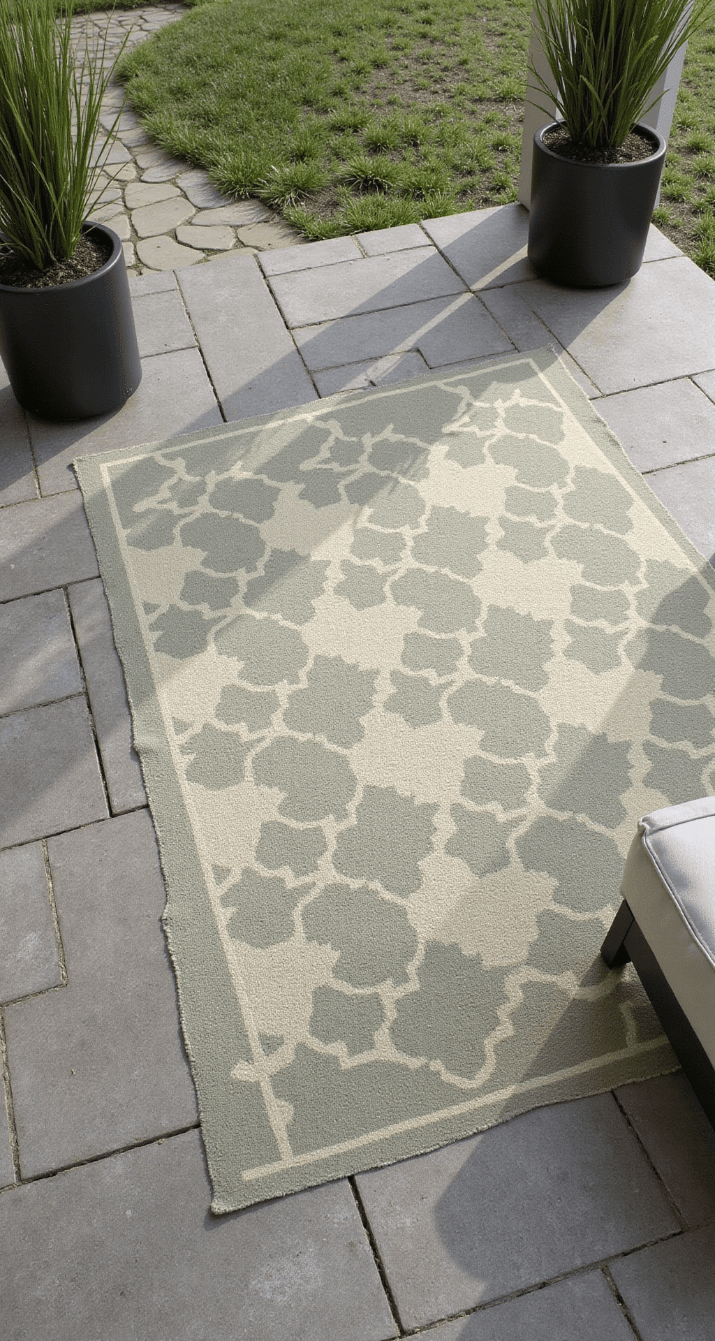 Modern Front Porch Decor Trends That'll Make Your Neighbors Actually Stop and Stare Overhead view of a herringbone-pattern concrete tile porch floor in warm gray with charcoal grout, featuring a large geometric outdoor rug in muted sage and cream, flanked by two black cylindrical planters with tall fountain grass, illuminated by afternoon light that enhances texture and contrast.