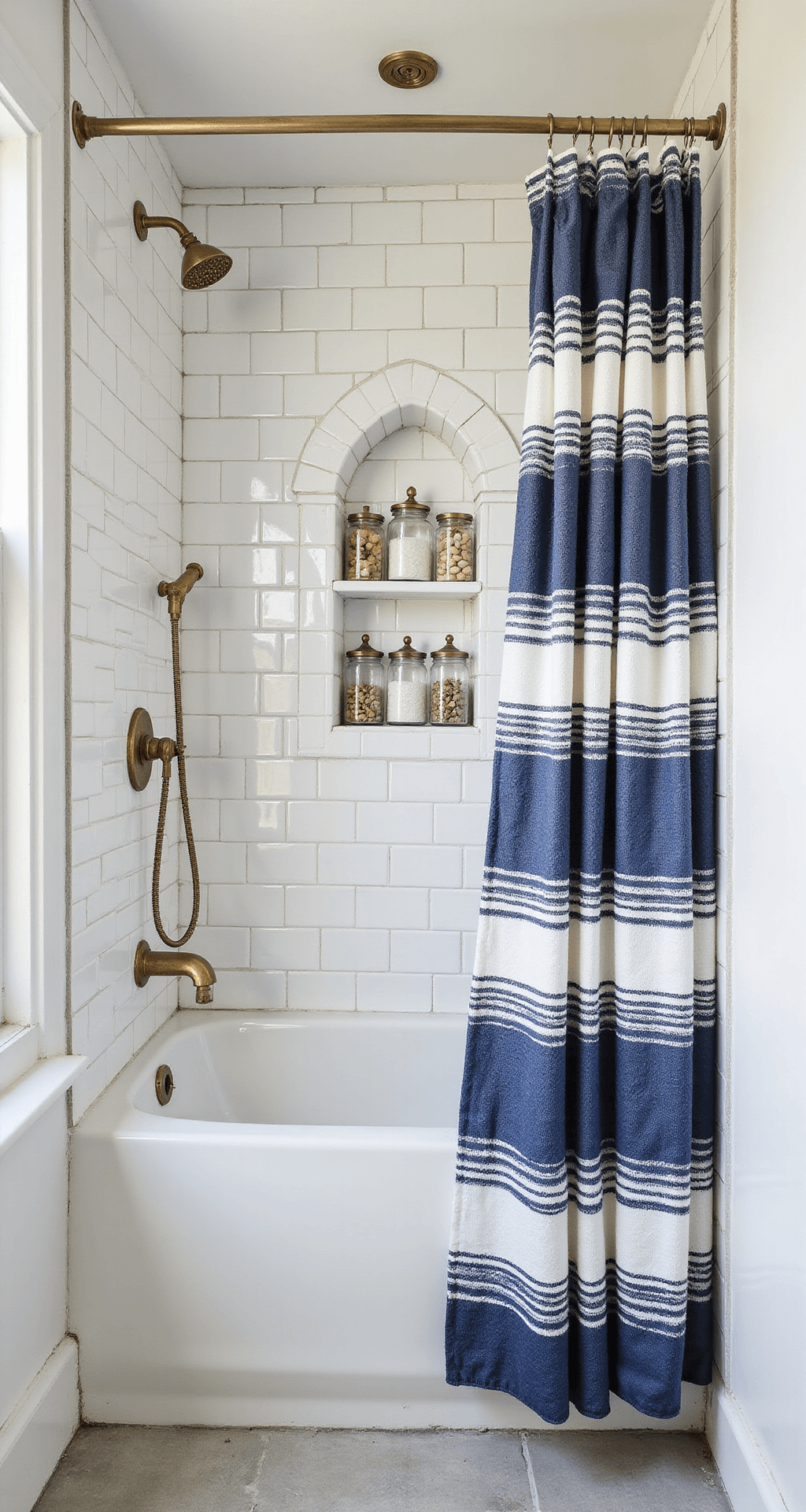 Coastal Bathroom Decor That'll Make Your Followers Double-Tap (And Actually Work in Real Life) Nautical coastal bathroom shower area featuring white subway tile with dark grout, navy and white striped linen shower curtain, vintage brass fixtures, and glass apothecary jars, all illuminated by soft morning light.